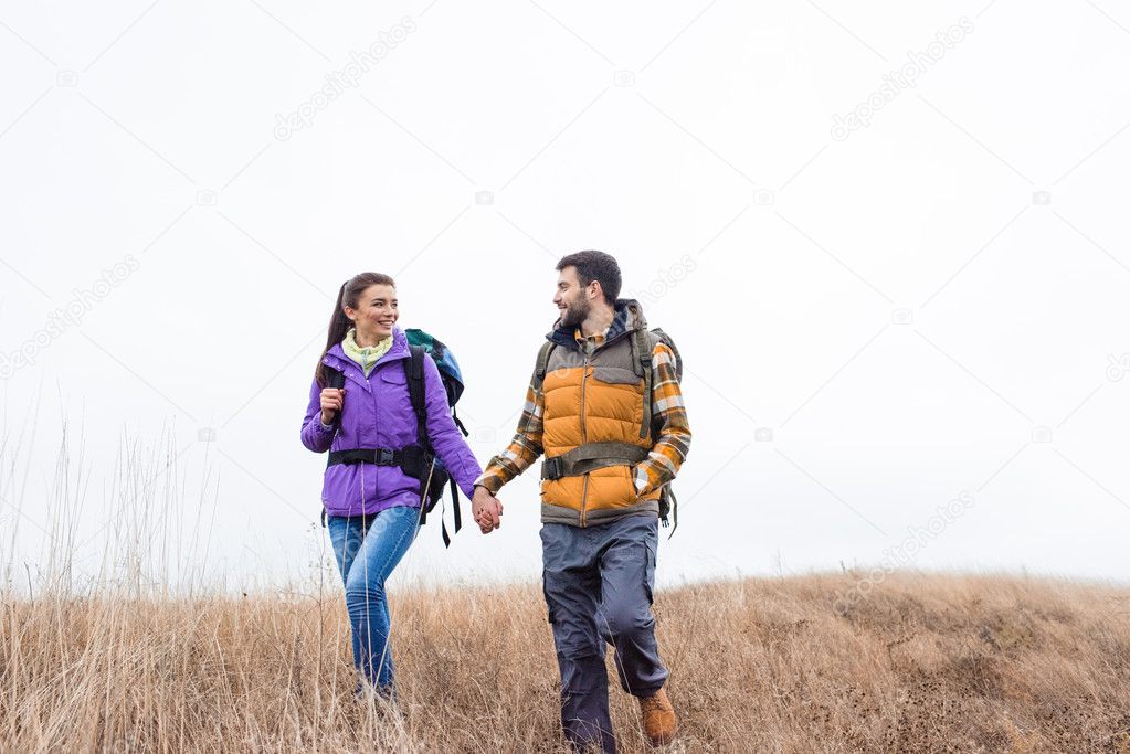 Smiling couple with backpacks walking in grass 