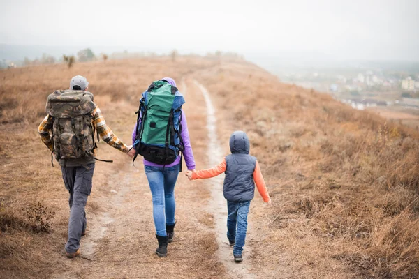 Family with backpacks walking on rural path — Stock fotografie