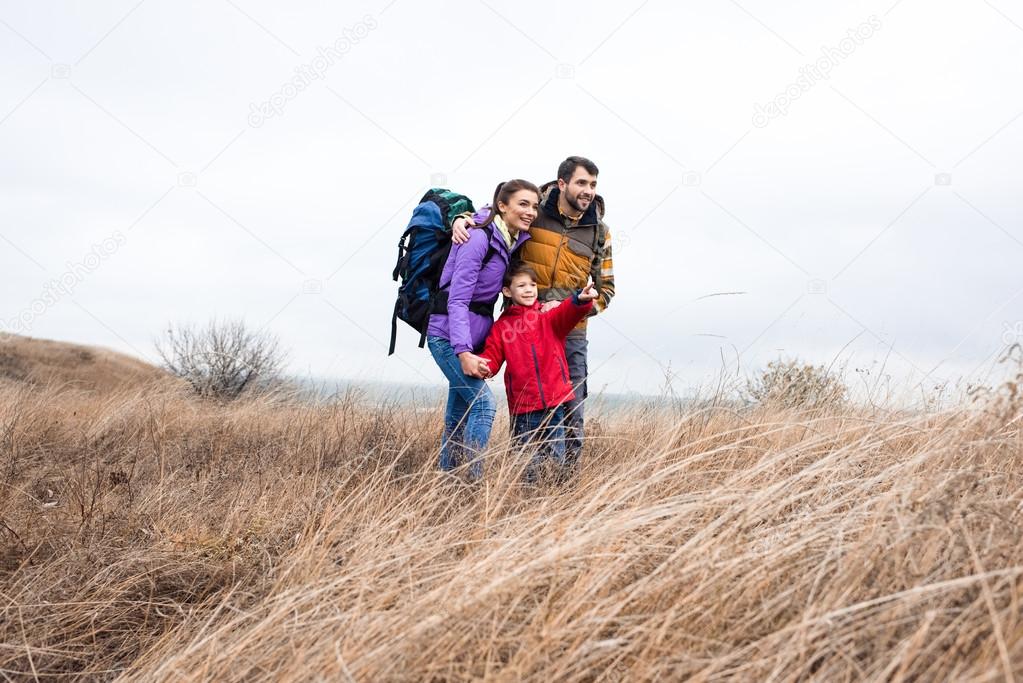 Happy family with backpacks standing in grass 