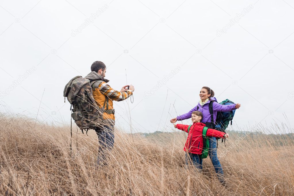 Man photographing wife and son with backpacks