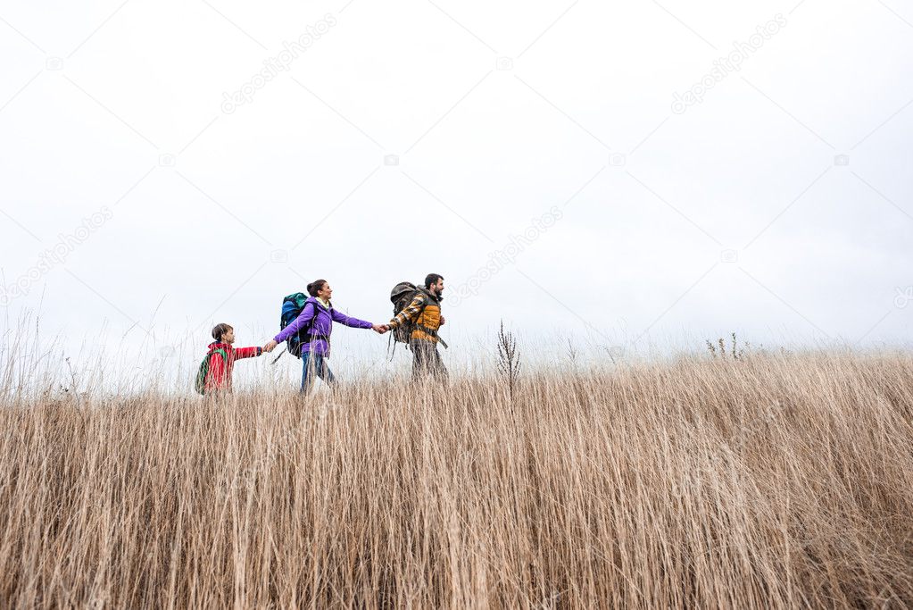 Happy family with backpacks walking in grass