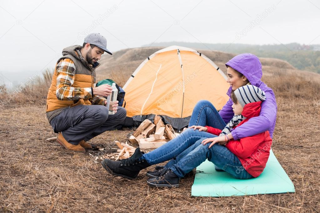 Happy young family sitting near tent
