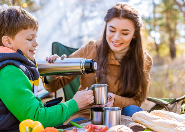 Happy mother pouring tea to son