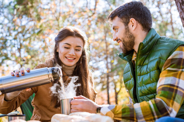 Smiling woman pouring tea from thermos