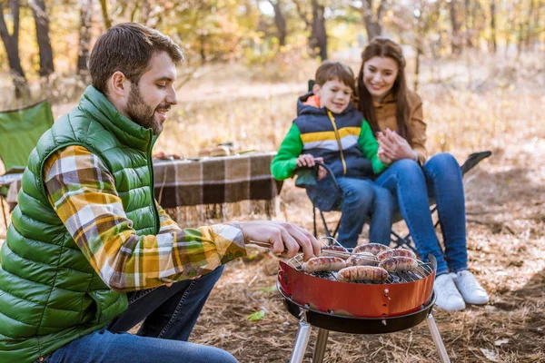 Padres alegres con su hijo asando salchichas — Foto de Stock