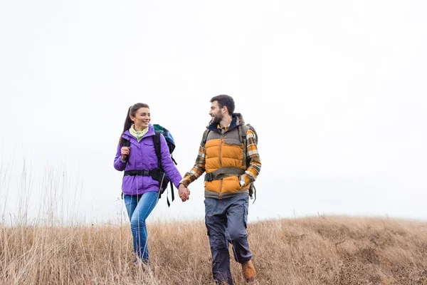 Coppia sorridente con zaini che camminano nell'erba — Foto stock