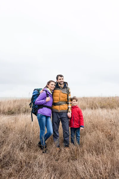 Happy family with backpacks standing in grass — Stock Photo