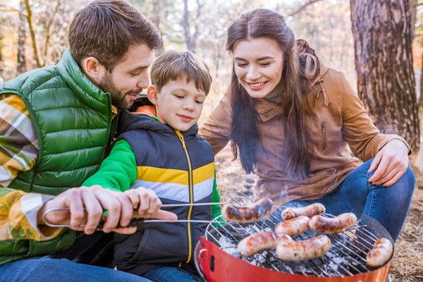 Pais alegres com filho grelhando salsichas — Fotografia de Stock