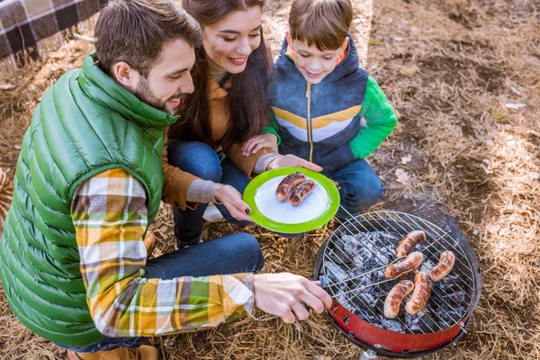 Cheerful parents with son grilling sausages — Stock Photo