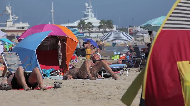 Playas españolas en Cataluña. La gente toma el sol en la playa bajo el sol caliente . — Vídeo de stock