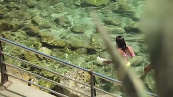 Ludzie kąpać i odpoczynek na plaży miejskiej. Dziewczyny w bikini idzie się wzdłuż brzegu morza w prowincjonalnym miasteczku Porto Cristo. Mallorca — Wideo stockowe