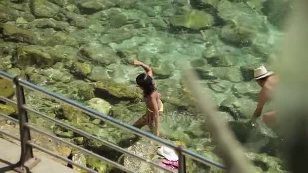 Люди купаются и отдыхают на городском пляже. Девушки в бикини идут вдоль берега моря в провинциальном городке Порто-Кристо. Майорка — стоковое видео