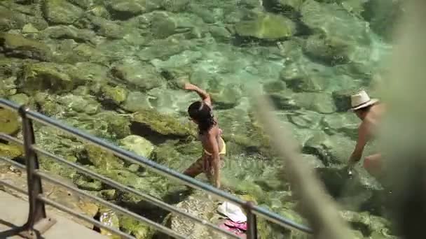 La gente se baña y descansa en la playa de la ciudad. Chicas en bikini van a lo largo de la orilla del mar en una ciudad provincial Porto Cristo. Mallorca — Vídeo de stock