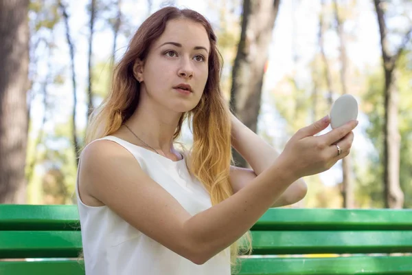 Жінка застосовує макіяж з дзеркалом в парку — стокове фото
