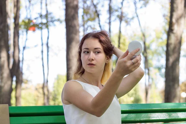 Woman applying make up with the mirror in the park — Stock Photo, Image