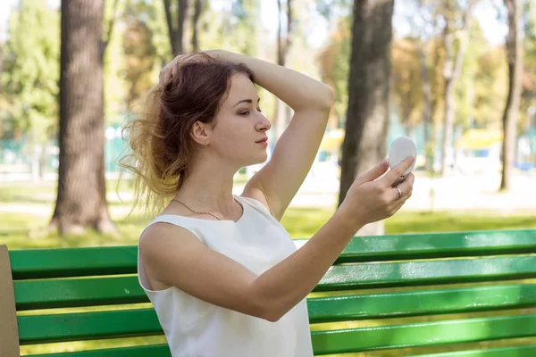 Woman applying make up with the mirror in the park — Stock Photo, Image