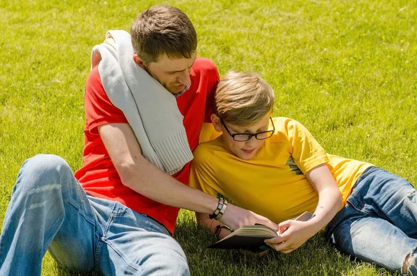 Joven hombre está leyendo un libro con adolescente Imágenes De Stock Sin Royalties Gratis