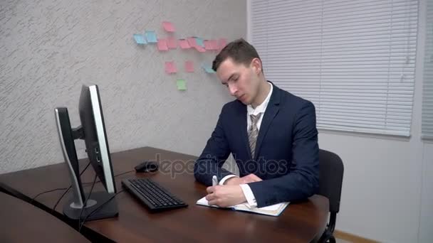 Молодой человек делает заметки в своем блокноте в офисе — стоковое видео