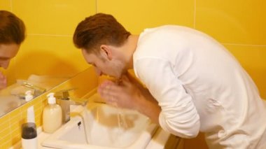 Genç adam banyoda yüzünü yıkıyor.