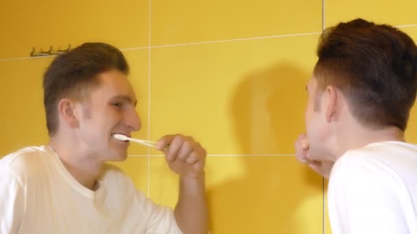 Νεαρός άνδρας, βουρτσίζετε τα δόντια του μπροστά από τον καθρέφτη — Αρχείο Βίντεο
