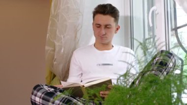 Kitap okuma ve pencere kenarında oturan genç adam