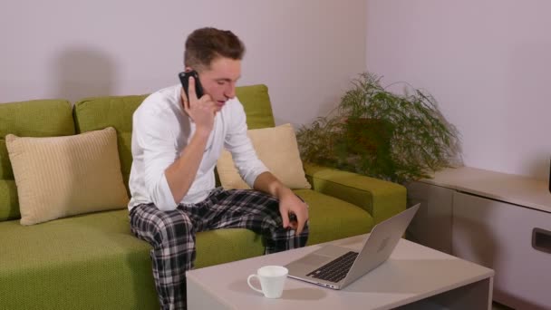 Mladý muž mluvil po telefonu a pomocí přenosného počítače ve svém obývacím pokoji — Stock video
