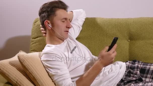 Junger Mann hört Musik auf dem Sofa — Stockvideo