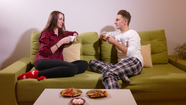 Happy young couplesitting on the sofa and drinking tea in the living room — Stock Video