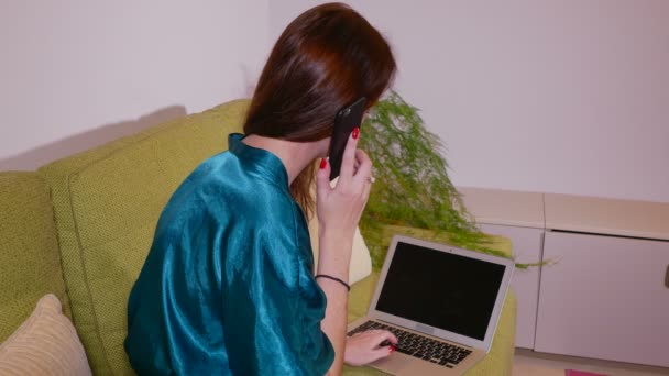 Nahaufnahme einer jungen Frau, die mit Laptop arbeitet und zu Hause telefoniert — Stockvideo
