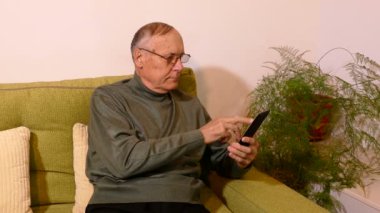 Oturma odasında kanepede oturan ve telefonunu kullanarak ihtiyar