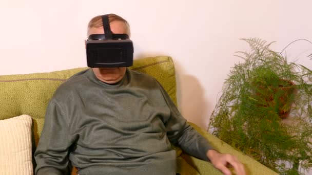 Vieil homme assis sur le canapé dans le salon et utilisant des lunettes virtuelles — Video