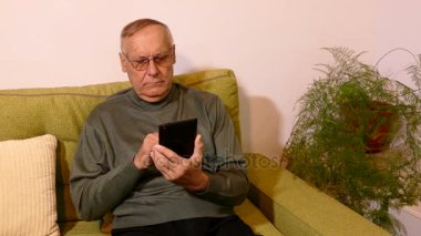 Oturma odasında kanepede oturan ve onun tableti kullanmak ihtiyar