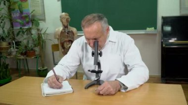 Mikroskop ve sınıfta not almak ile çalışan bir üniversite profesörü