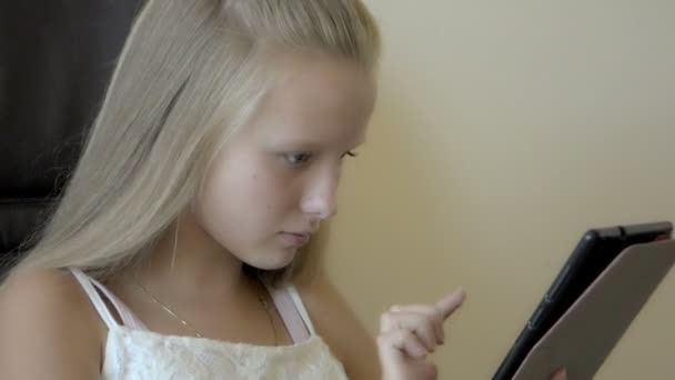 Крупный план девочки-подростка, сидящей и играющей с планшетом — стоковое видео