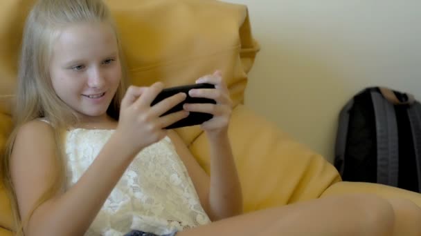 Chica adolescente sentada y disfrutando jugando con el teléfono inteligente — Vídeos de Stock