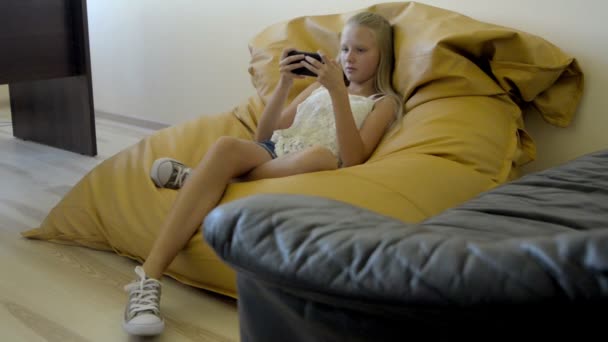 Menina adolescente sentada na poltrona e brincando com o celular — Vídeo de Stock