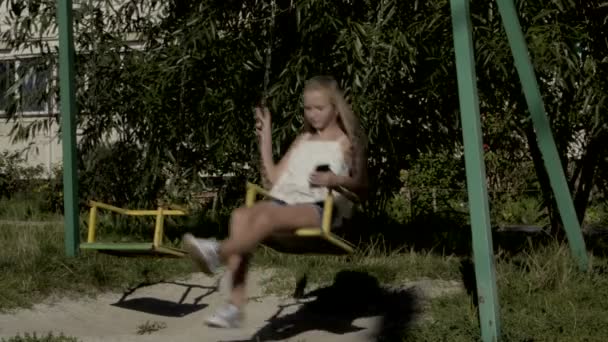 Dospívající dívka poslouchá hudbu a zpěv na houpačce — Stock video