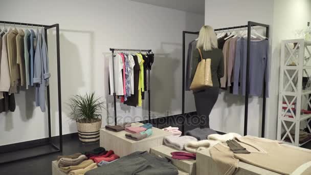 Mujer joven recogiendo ropa en la boutique — Vídeos de Stock