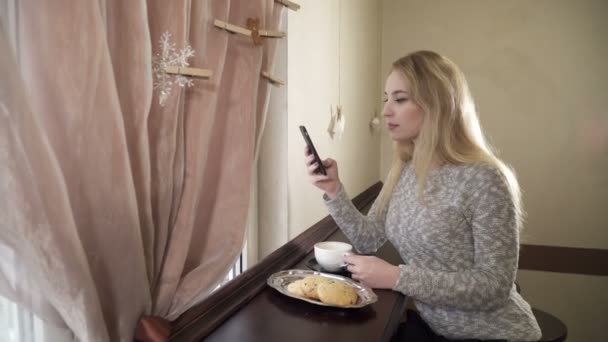 Молодая женщина, сидящая в кафе и пользующаяся телефоном — стоковое видео
