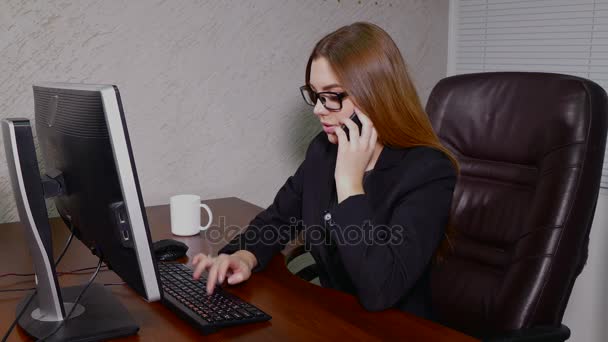 Mujer joven trabajando en la computadora y hablando por teléfono — Vídeos de Stock