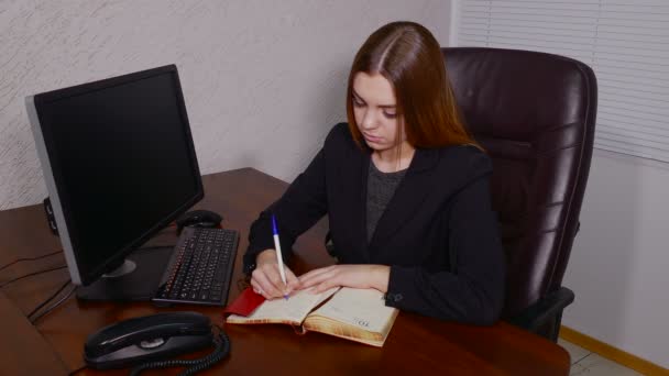 Fiatal nő jegyzetelés a jegyzetfüzet, előtt ő képernyő office — Stock videók