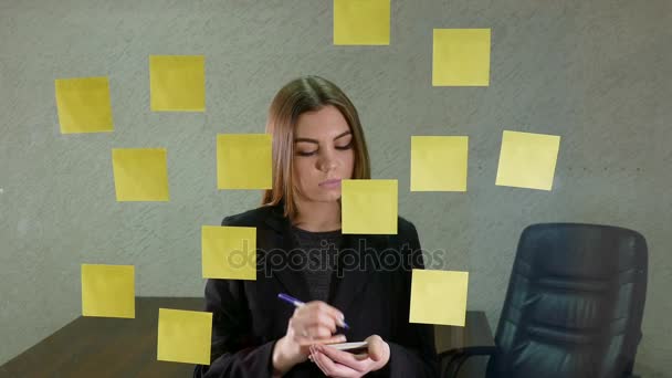 Młoda kobieta, pisanie na karteczki i trzymać je na szklanym ekranie — Wideo stockowe