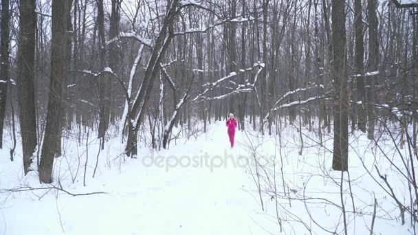Νεαρή ξανθιά γυναίκα στο κοστούμι αθλητισμού τρέχει στο δάσος του χειμώνα — Αρχείο Βίντεο
