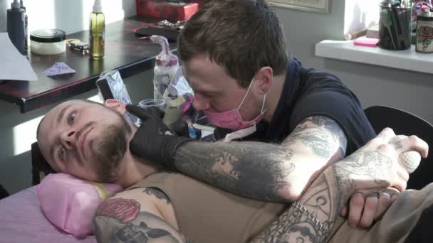Tatooer em máscara está fazendo tatoo de animal no pescoço do homem — Vídeo de Stock