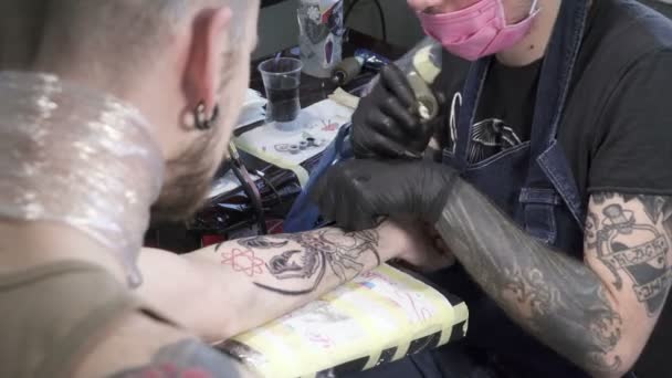 Татуировщик в маске и черных перчатках делает тату из насекомых на руке — стоковое видео