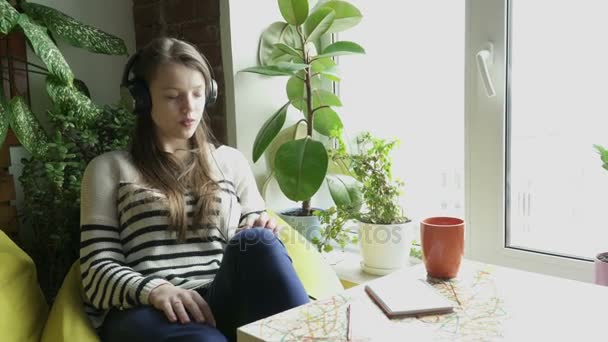 Девочка-подросток, сидящая в наушниках и лизующая музыку — стоковое видео