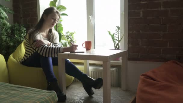 Tiener meisje zitten aan de tafel en het maken van notities — Stockvideo