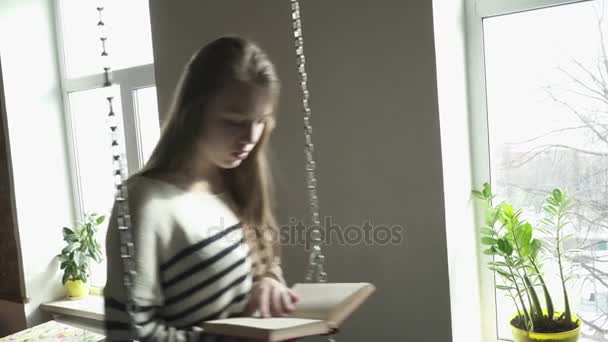 Крупный план девочки-подростка, сидящей на свинде и читающей книгу — стоковое видео