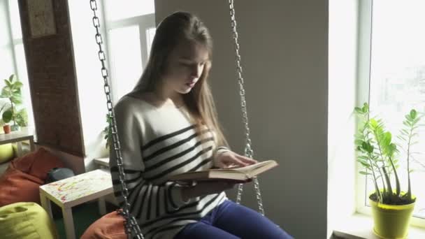 Teenager Mädchen sitzt auf Swinde und liest ein Buch — Stockvideo