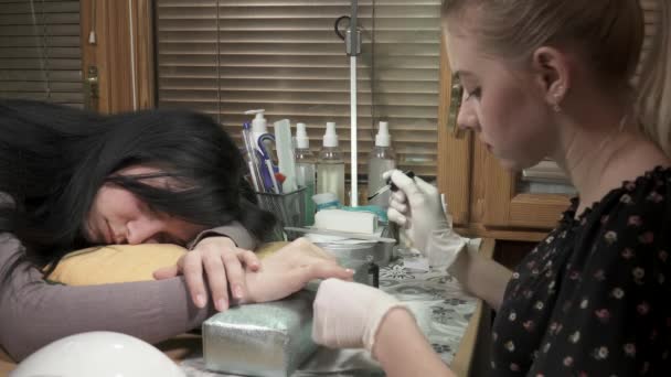 Молодой мастер маникюра делает маникюр, пока ее клиент спит — стоковое видео